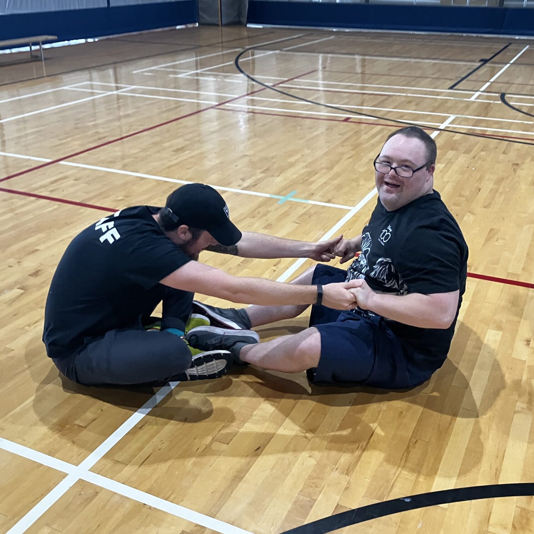 A Thrive participant smiles while helping a staff member stretch on the floor on the the court.