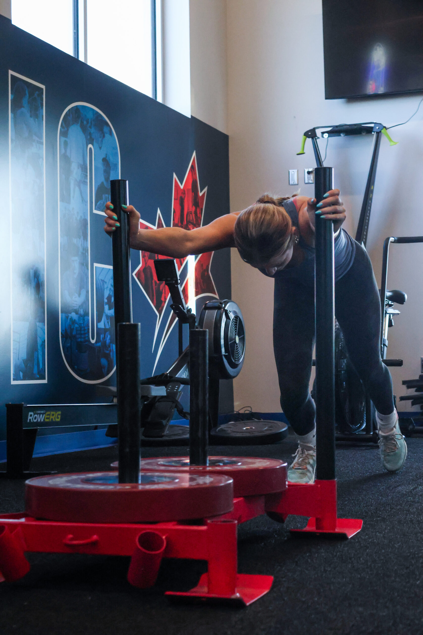 A female athlete pushing stacks of weights across the floor.