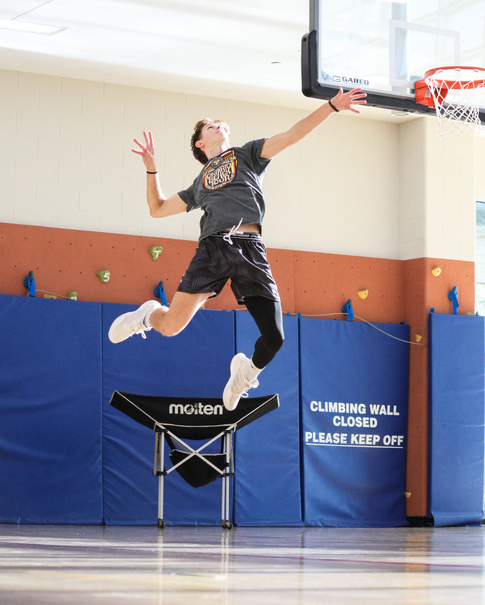 A male volleyball student in mid-air about to hit the ball.
