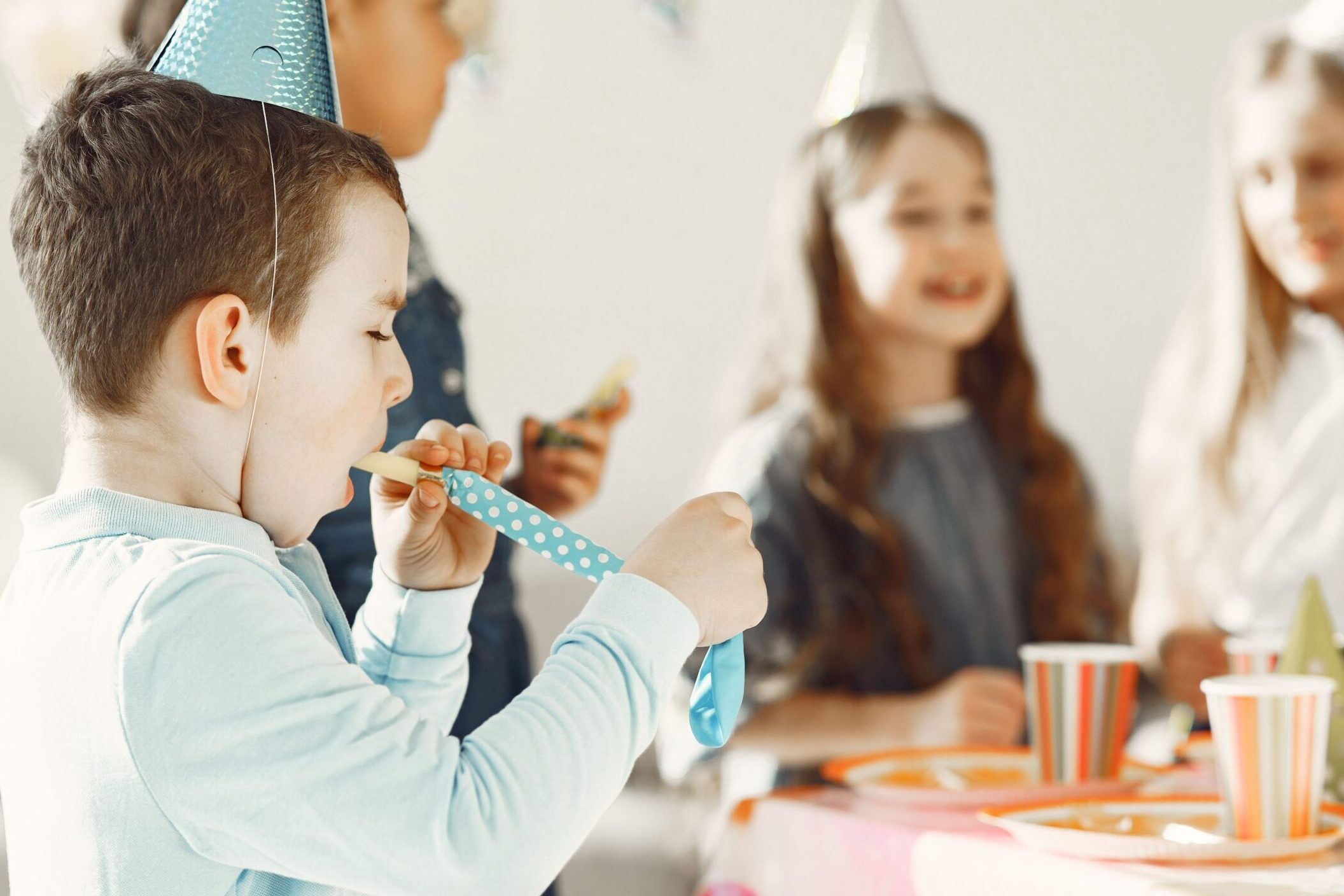 A boy putting a noisemaker in his mouth during a birthday party.