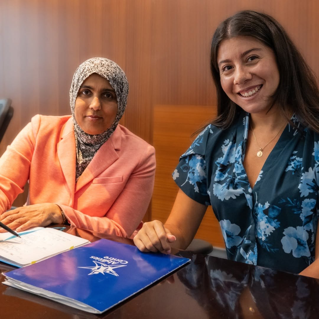Two women post while sitting at a table.