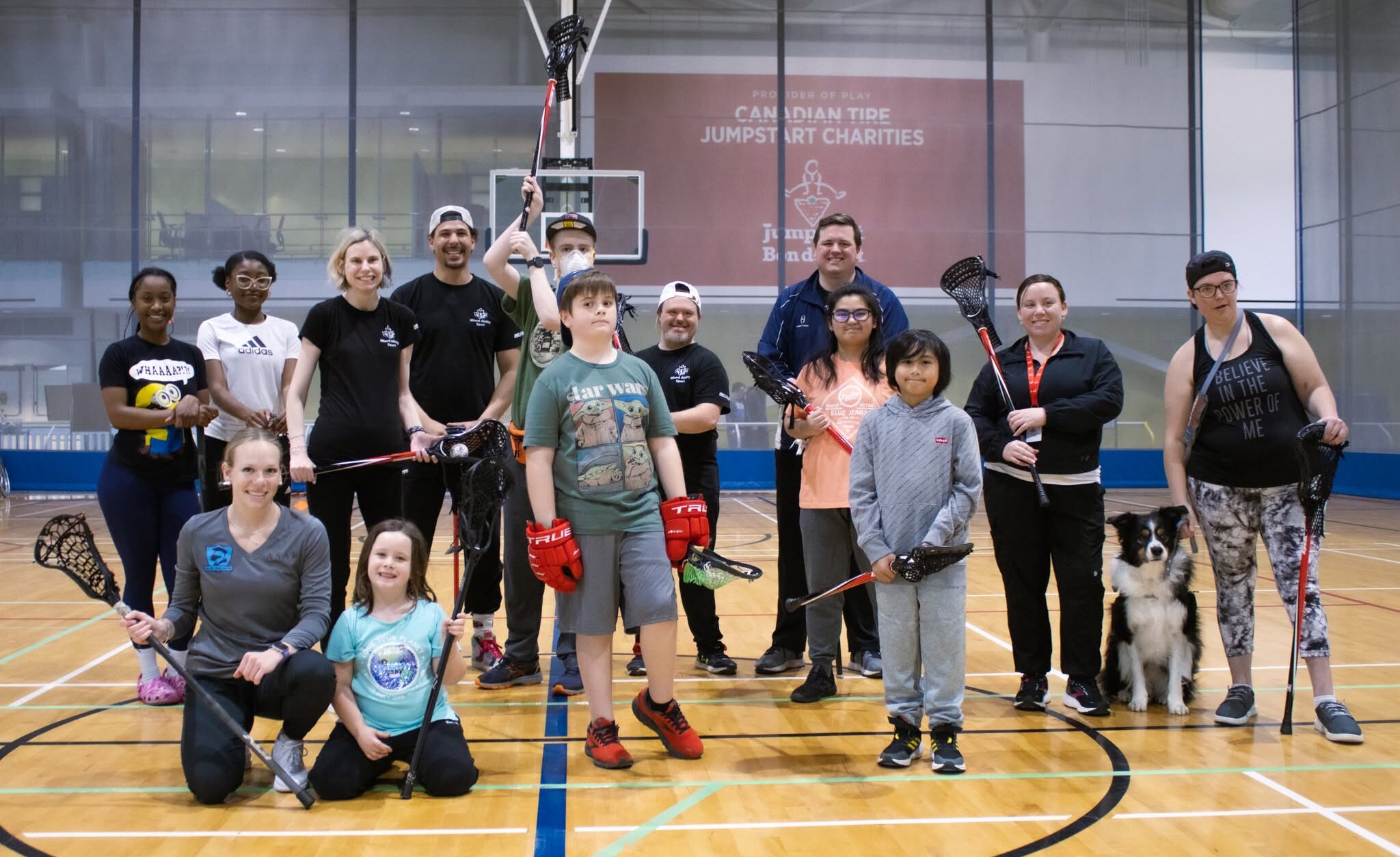 A group of participants pose while holding thier lacrosse sticks on the court.