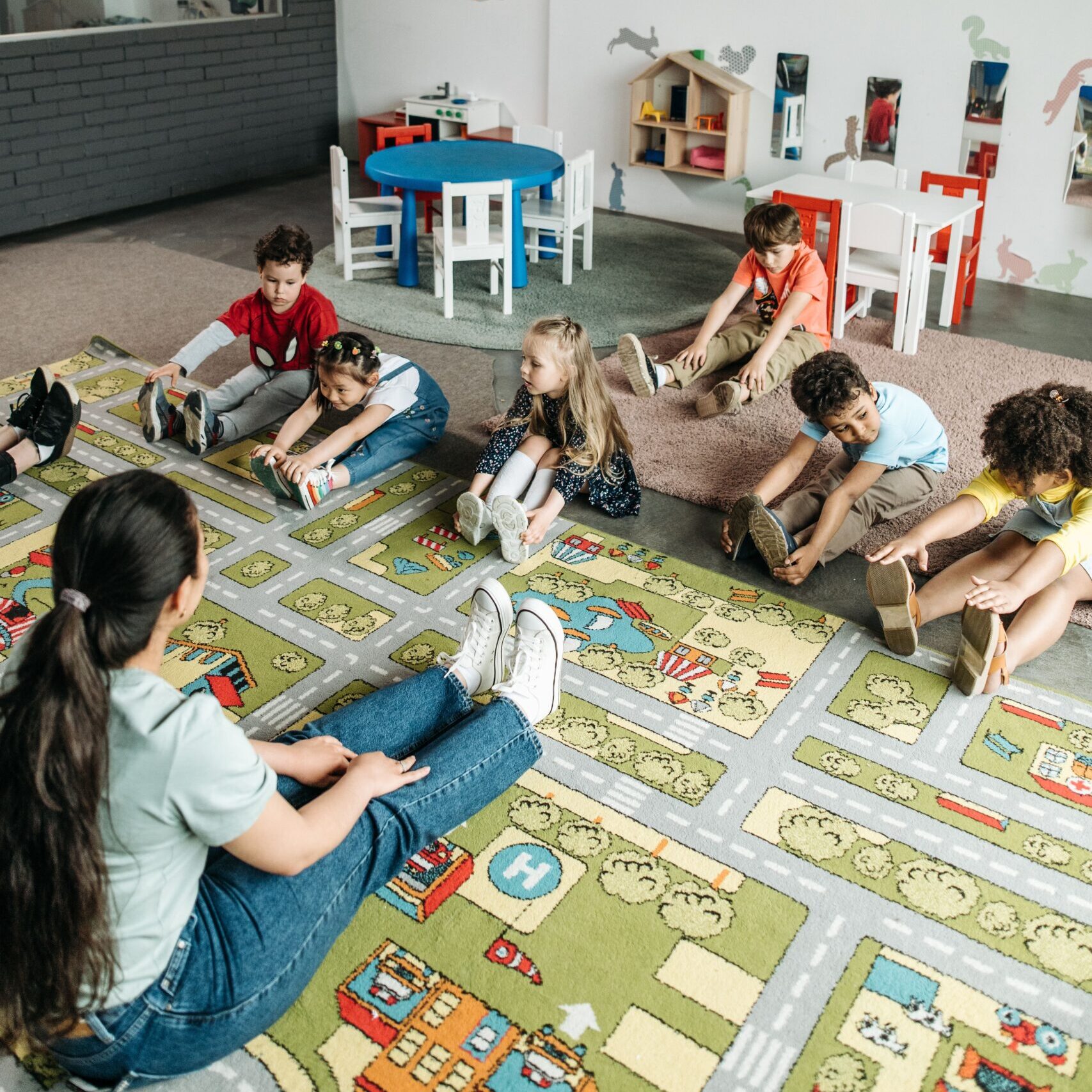 A teacher and her young students stretch on the floor.