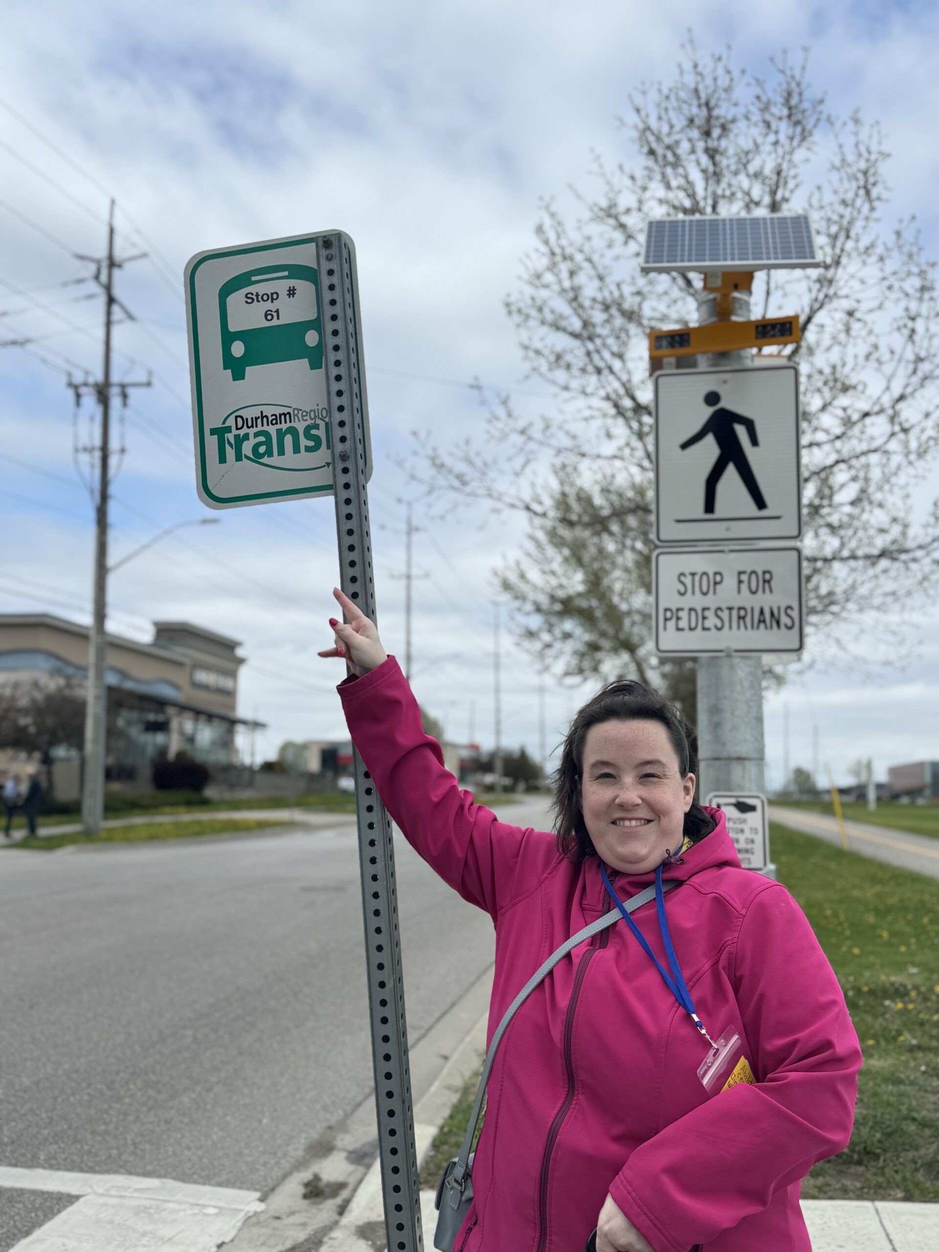 A woman smiles as she points up to the Durham Region Transit bus stop.