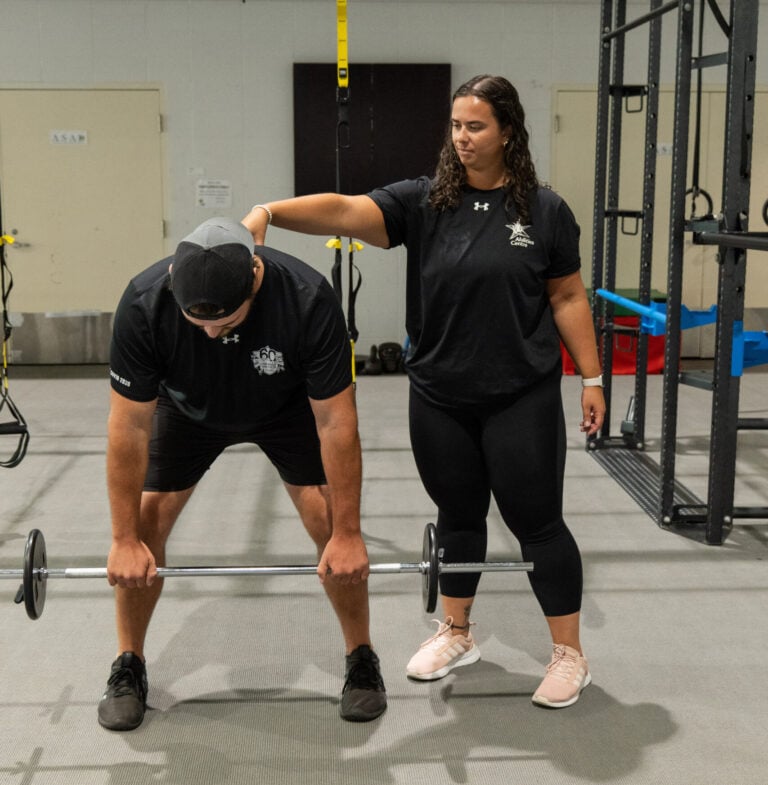 A personal trainer helping a client fix their form as they lift weights.