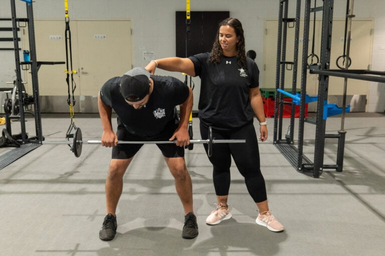 A personal trainer telling a client how to fix their form as they lift weights.